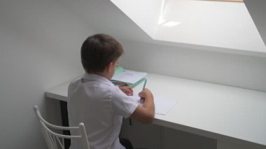 Küçük okul çocuğu ödev yapıyor, kalemle deftere yazıyor.