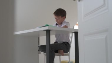 Küçük okul çocuğu ödev yapıyor, kalemle deftere yazıyor.
