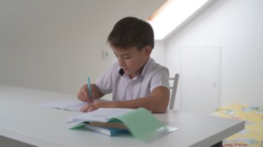 Küçük okul çocuğu ödev yapıyor, kalemle deftere yazıyor.