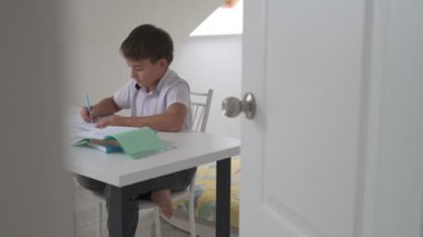 Küçük okul çocuğu ödev yapıyor, kalemle deftere yazıyor.