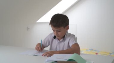 Küçük okul çocuğu ödev yapıyor, kalemle deftere yazıyor.