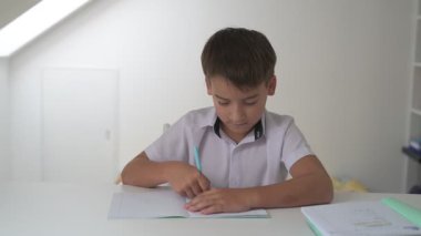 Küçük okul çocuğu ödev yapıyor, kalemle deftere yazıyor.