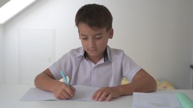 Küçük okul çocuğu ödev yapıyor, kalemle deftere yazıyor.