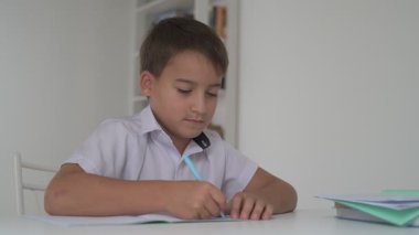 Küçük okul çocuğu ödev yapıyor, kalemle deftere yazıyor.