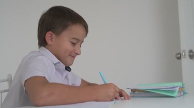 Küçük okul çocuğu ödev yapıyor, kalemle deftere yazıyor.