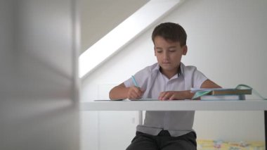 Küçük okul çocuğu ödev yapıyor, kalemle deftere yazıyor.