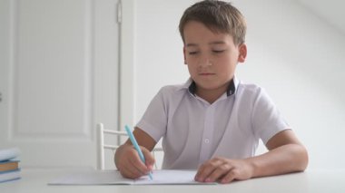 Küçük okul çocuğu ödev yapıyor, kalemle deftere yazıyor.