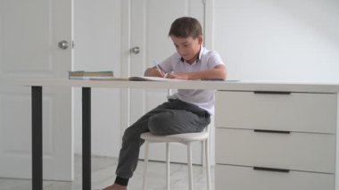 Küçük okul çocuğu ödev yapıyor, kalemle deftere yazıyor.