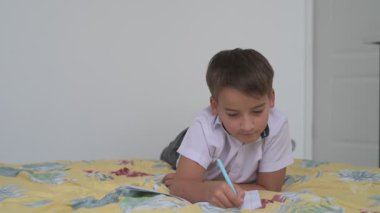 Küçük okul çocuğu ödev yapıyor, kalemle deftere yazıyor.