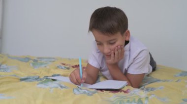 Küçük okul çocuğu ödev yapıyor, kalemle deftere yazıyor.