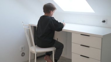 Küçük okul çocuğu ödev yapıyor, kalemle deftere yazıyor.