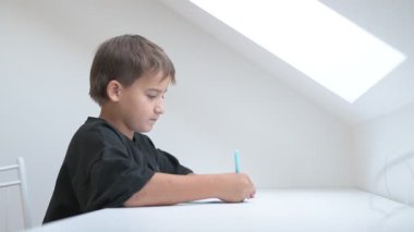 Küçük okul çocuğu ödev yapıyor, kalemle deftere yazıyor.