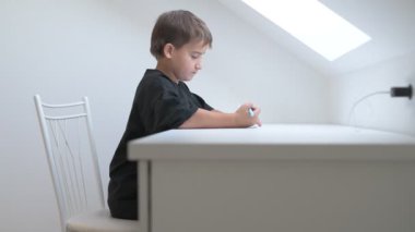 Küçük okul çocuğu ödev yapıyor, kalemle deftere yazıyor.