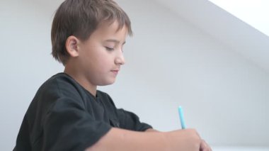 Küçük okul çocuğu ödev yapıyor, kalemle deftere yazıyor.