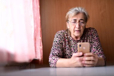 Evde cep telefonu olan yaşlı bir kadın.