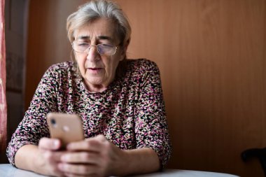 Evde cep telefonu olan yaşlı bir kadın.