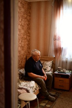 Kanepede oturmuş televizyon izleyen üzgün bir Sovyet ihtiyarın portresi.