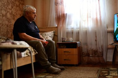 Kanepede oturmuş televizyon izleyen üzgün bir Sovyet ihtiyarın portresi.