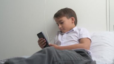 Küçük okul çocuğu evde yatarken cep telefonu ekranını seyretmeye dalmış.