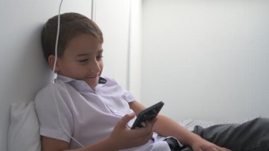 Küçük okul çocuğu evde yatarken cep telefonu ekranını seyretmeye dalmış.
