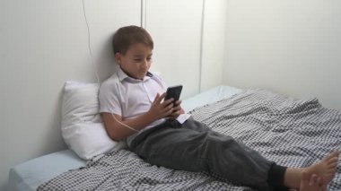 Küçük okul çocuğu evde yatarken cep telefonu ekranını seyretmeye dalmış.