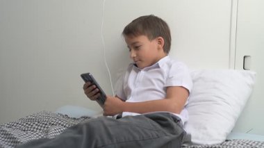 Küçük okul çocuğu evde yatarken cep telefonu ekranını seyretmeye dalmış.