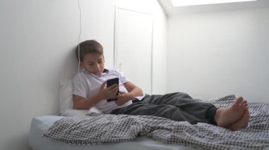 Küçük okul çocuğu evde yatarken cep telefonu ekranını seyretmeye dalmış.