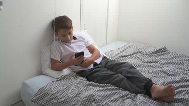 Küçük okul çocuğu evde yatarken cep telefonu ekranını seyretmeye dalmış.