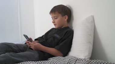 Küçük okul çocuğu evde yatarken cep telefonu ekranını seyretmeye dalmış.