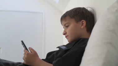 Küçük okul çocuğu evde yatarken cep telefonu ekranını seyretmeye dalmış.
