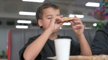 Küçük beyaz çocuk annesiyle pizzacıda pizza yiyor.