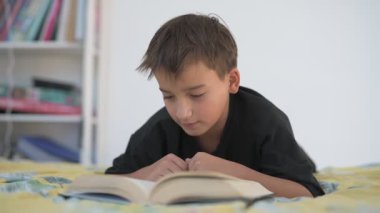 Küçük okul çocuğu yatağında kitap okuyor.
