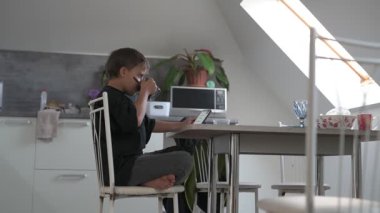 Okul çocuğu okuldan önce mutfakta kahvaltı hazırlıyor, kahve yapıyor ve cep telefonunu kontrol ediyor.