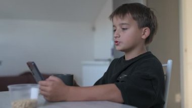 Okul çocuğu okuldan önce mutfakta kahvaltı hazırlıyor, kahve yapıyor ve cep telefonunu kontrol ediyor.