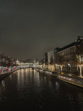 Gece manzaralı ünlü Amsterdam kanalları, kanaldaki tekneler ve kanal kenarındaki evler