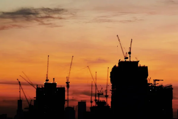 Silhouette building crane and buildings under construction against evening sky.