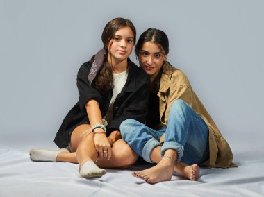 Yerde oturmuş kameraya bakan iki gencin portresi.