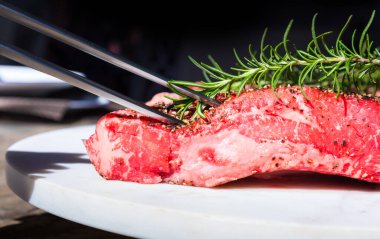 Çiğ Wagyu bifteği ve beyaz bir tabakta biberiye dalı.