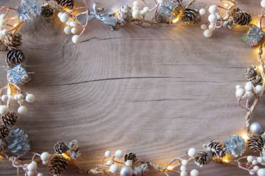 Işıklı kış Noel arkaplanı. Hediyeli süsleme, kahverengi kuru koni, doğal ahşap arka planda beyaz böğürtlen. Boşluğu kopyala.  