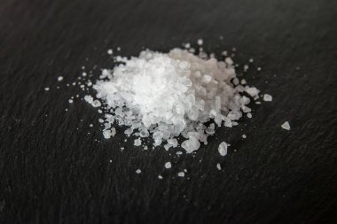 Yemeği pişirmek için tuz kristalleri. Siyah doğal bir arkaplanda deniz tuzu yığını. 