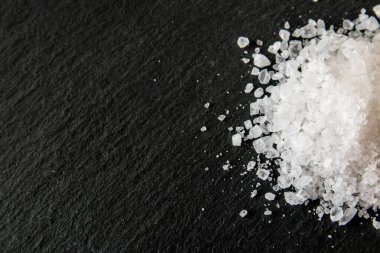 Yemeği pişirmek için tuz kristalleri. Siyah doğal bir arkaplanda deniz tuzu yığını. 