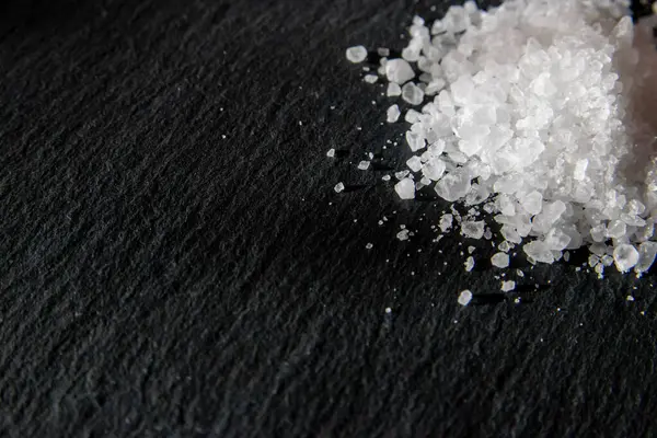 Yemeği pişirmek için tuz kristalleri. Siyah doğal bir arkaplanda deniz tuzu yığını. 
