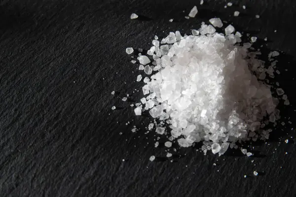 Yemeği pişirmek için tuz kristalleri. Siyah doğal bir arkaplanda deniz tuzu yığını. 