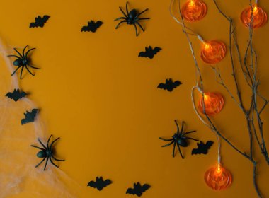 Cadılar Bayramı süslemeleri, balkabakları, yarasalar, ağ, turuncu arka planda böcekler. Kopya alanı olan parti tebrik kartı. Düz yatış, üst görünüm.