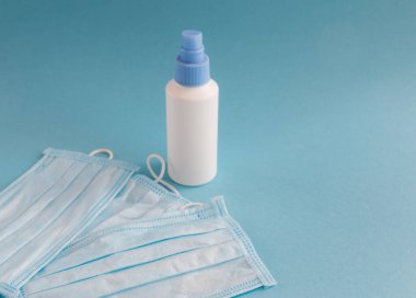 Dezenfeksiyon spreyi ve tıbbi maske. Mavi arka planda, mesaj için yer var. Kirliliğe ve virüs korumasına karşı antibakteriyel. Covid-19 - Coronavirüs enfeksiyonu. 