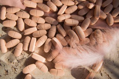 Pink pills or vitamins on the natural wood background with pink silk fabric and feather in summer day.  clipart