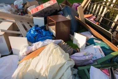 Ev yakınlarındaki bir şehirde çok fazla atık var. Eski ahşap mobilyaları, oyuncakları, kutuları, sokakta plastik torbaları ve Almanya 'da bahar güneşli çöplük gününde yeşil çimenleri olan büyük bir çöp.. 