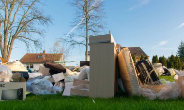 Ev yakınlarındaki bir şehirde çok fazla atık var. Eski ahşap mobilyaları, oyuncakları, kutuları, sokakta plastik torbaları ve Almanya 'da bahar güneşli çöplük gününde yeşil çimenleri olan büyük bir çöp.. 