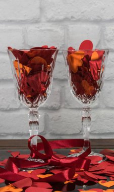 Kırmızı kağıt kalpler ve iki kadeh şampanyadaki kırmızı bant taştan yapılı arka planda ışıkla. Sevgililer Günü ya da düğün günü için aşk işareti.