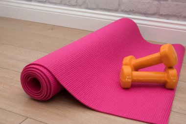 Spor salonunda pembe yoga minderinde iki turuncu dambıl. Yaz zamanı eğitim, spor ve etkinlik araçları.